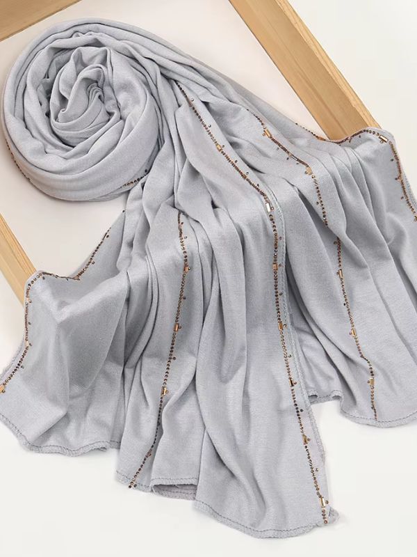 Hijab jersey premium strassé gris perle, enroulé et drapé dans un cadre en bois, lignes de strass cuivrés sur toute la longueur