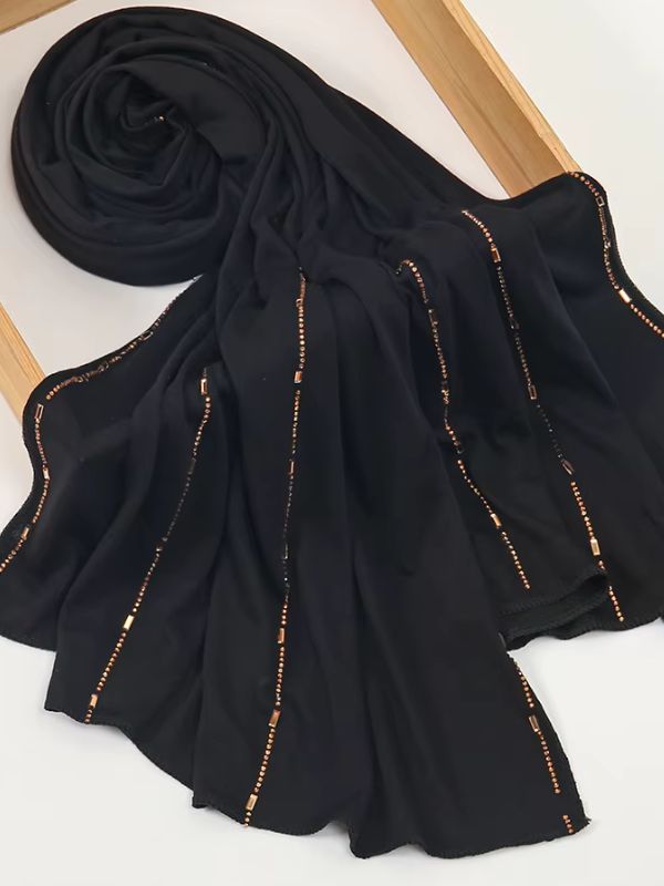 Hijab jersey premium strassé noir, enroulé et drapé dans un cadre en bois, lignes de strass cuivrés et dorés sur toute la longueur