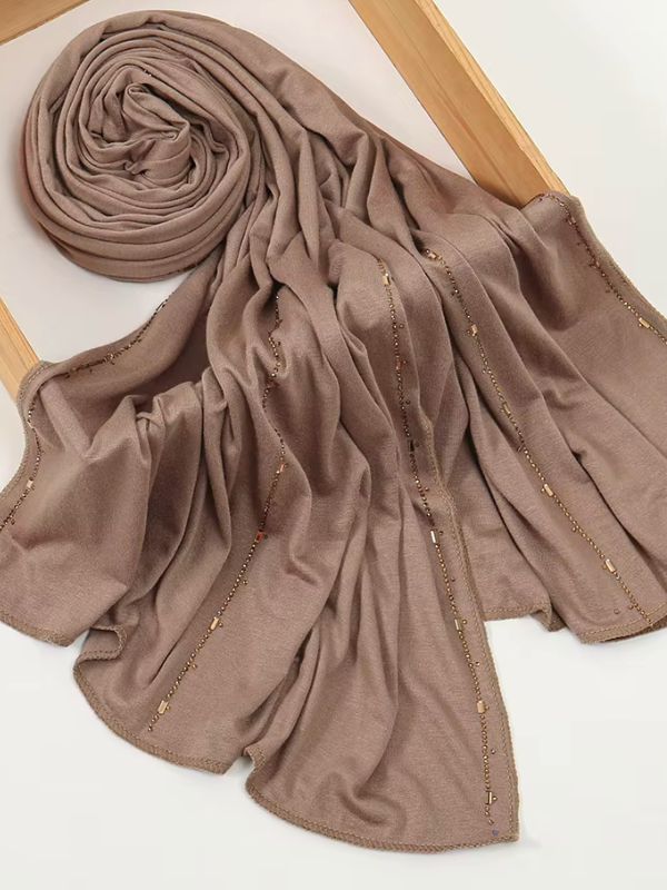 Hijab jersey premium strassé taupe rosé, enroulé et drapé dans un cadre en bois, lignes de strass bronze sur toute la longueur