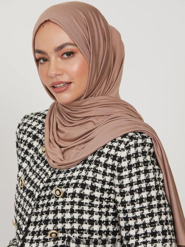 Femme portant un hijab en jersey de couleur taupe, accompagnée d'une veste à motifs pied-de-poule noir et blanc