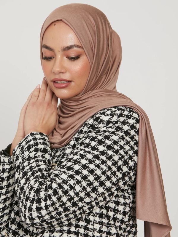 Femme portant un hijab en jersey de couleur taupe, accompagnée d'une veste à motifs pied-de-poule noir et blanc