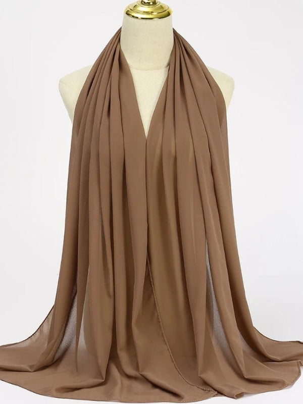 Un hijab marron en mousseline est élégamment drapé sur un mannequin. Le tissu fluide et légèrement transparent crée des plis délicats qui tombent gracieusement, ajoutant une touche de sophistication. La couleur marron douce offre une option neutre et polyvalente, idéale pour compléter une variété de tenues. Le hijab est soigneusement arrangé pour mettre en valeur la légèreté du tissu, accentuant sa capacité à être porté de manière confortable et stylée pour diverses occasions