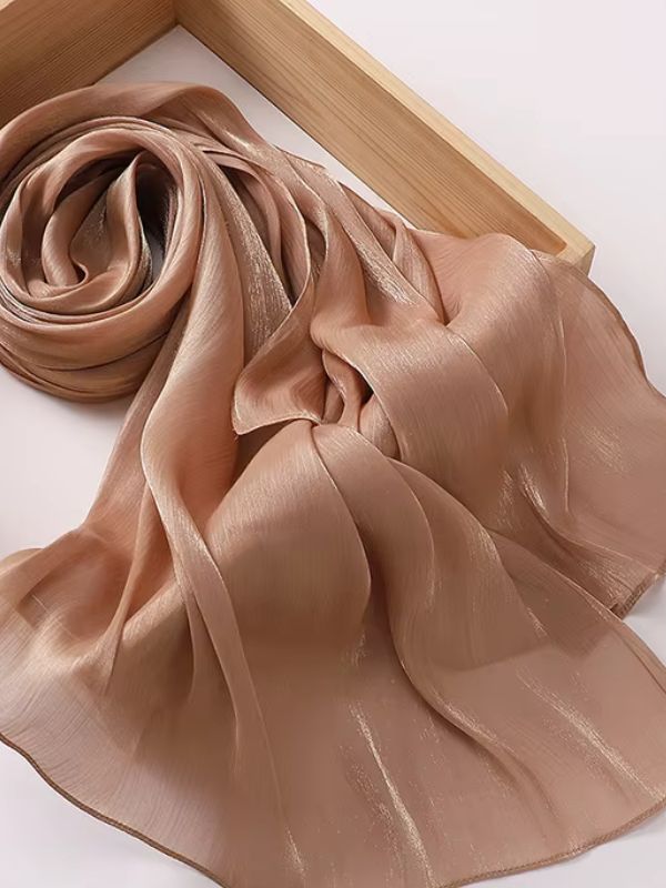 Hijab mousseline de soie froissée caramel doré aux reflets shimmer cuivrés, présenté enroulé et déplié sur un plateau en bois naturel