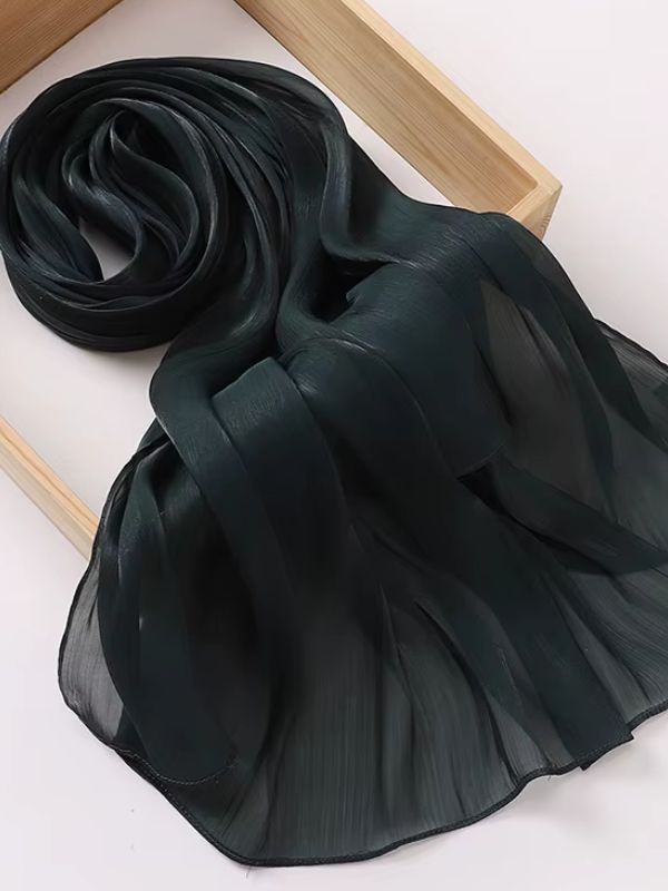 Hijab mousseline de soie froissée noire aux reflets shimmer soyeux, présenté enroulé sur un plateau en bois naturel