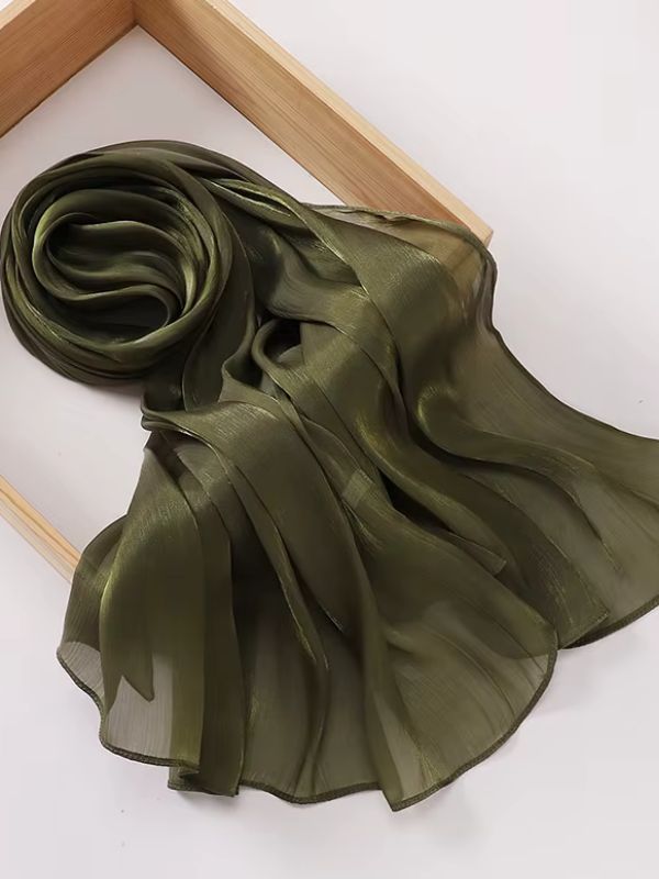 Hijab mousseline de soie froissée vert kaki aux reflets shimmer chauds, présenté enroulé et déplié sur un plateau en bois naturel