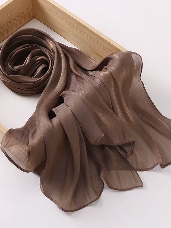 Hijab mousseline de soie froissée brun cannelle aux reflets shimmer dorés, présenté enroulé et déplié sur un plateau en bois naturel