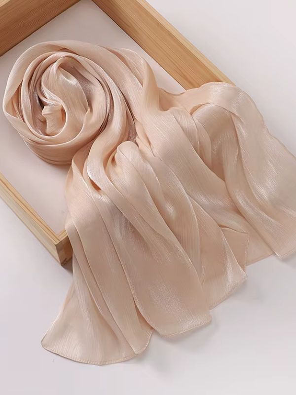 Hijab mousseline de soie froissée beige nude aux reflets shimmer dorés, présenté enroulé et déplié sur un plateau en bois naturel