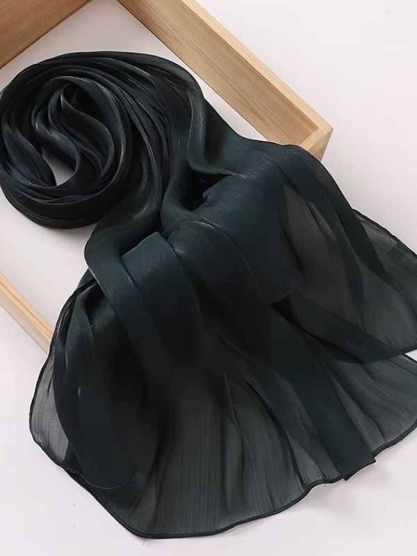 Hijab mousseline de soie froissée vert ivy profond aux reflets shimmer soyeux, présenté enroulé et déplié sur un plateau en bois naturel