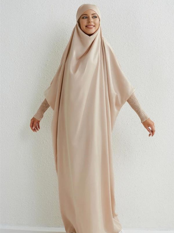 Femme portant un jilbab beige, posant de côté devant un fond neutre