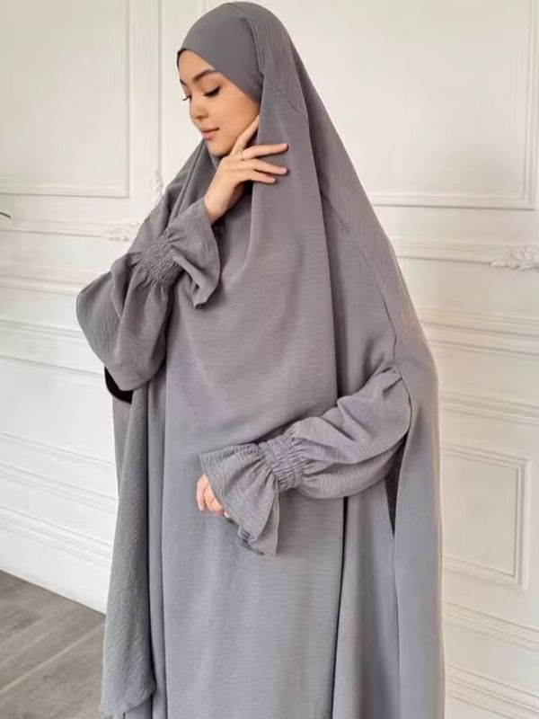 Jilbab femme gris vu de trois quarts, capuche drapée sur les épaules, manches larges aux poignets froncés