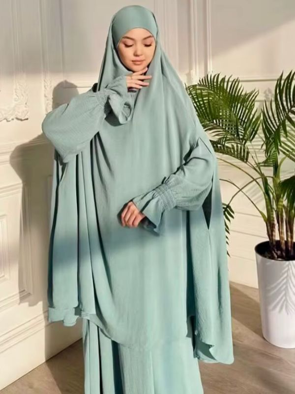 Jilbab femme vert d'eau devant un palmier en pot, grand haut ample à capuche et jupe longue, vue de face