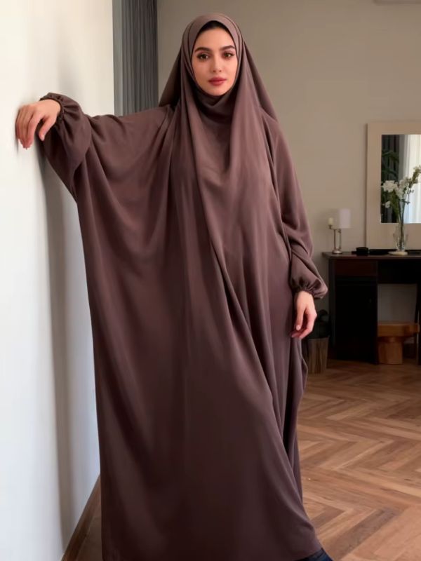 Jilbab femme marron, bras appuyé contre un mur, manche ample aux poignets froncés, vue de trois quarts