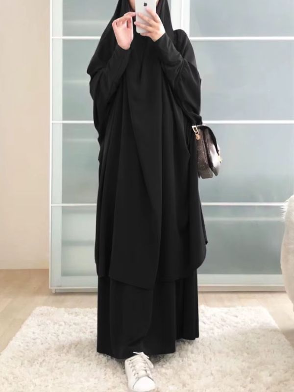 Une femme porte un jilbab noir ample et fluide dans un intérieur lumineux.