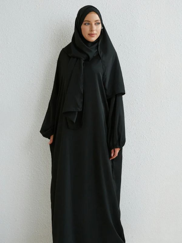 Femme vêtue d'un jilbab noir, simple et élégant, avec une coupe ample qui met en valeur la fluidité du tissu et un hijab assorti pour un look sobre et classique