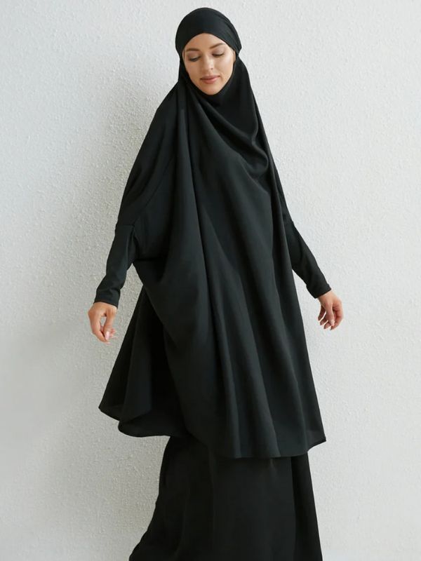 Femme vêtue d'un jilbab noir, simple et élégant, avec une coupe ample qui met en valeur la fluidité du tissu et un hijab assorti pour un look sobre et classique