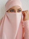 Gros plan sur le visage d&#39;une femme portant un jilbab rose clair avec un voile couvrant partiellement son visage, mettant en valeur ses yeux bleus