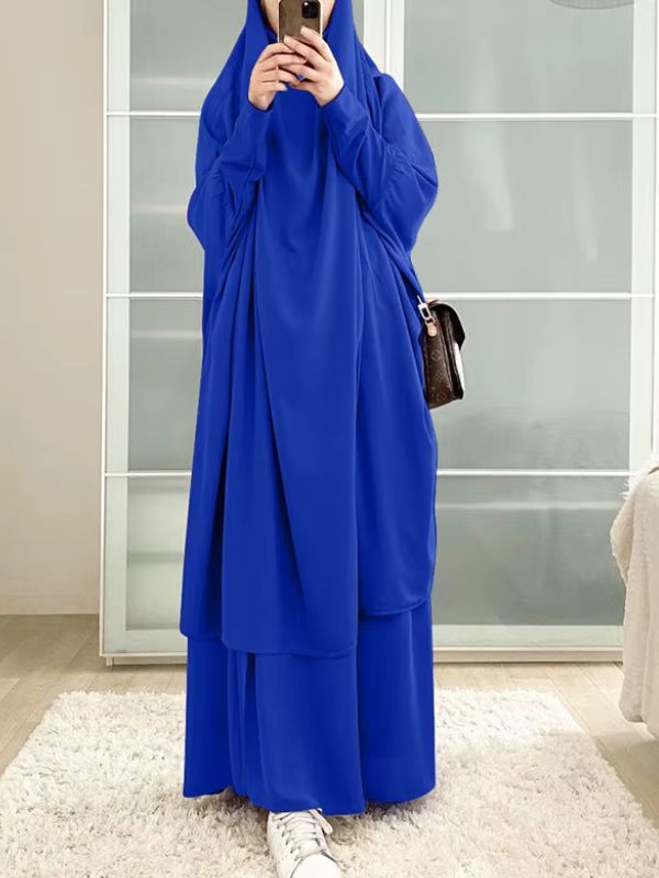 Une femme porte un jilbab bleu saphir ample et fluide dans un intérieur lumineux.