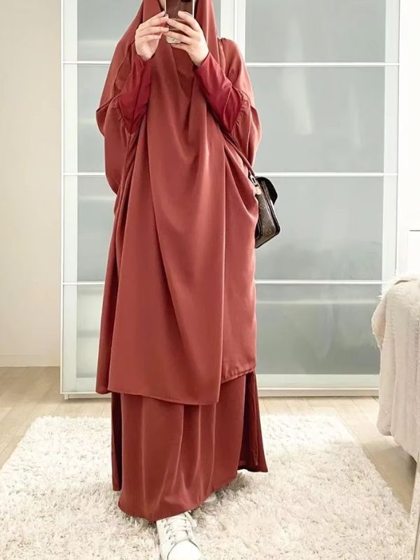 Une femme photographie son reflet en portant un jilbab couleur brun sienne long et ample avec des baskets blanches.