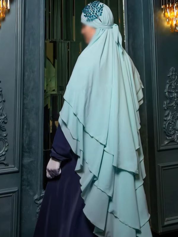 Une femme porte un khimar bleu ciel plissé avec trois voiles superposés