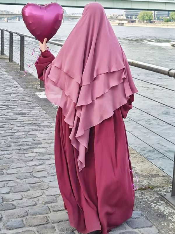 Une femme porte un khimar rose et tient un ballon en forme de cœur