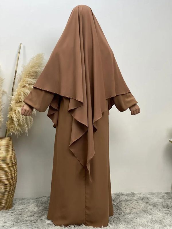 Femme portant un khimar long brun sable, vue de dos, posant dans un cadre minimaliste avec des décorations naturelles