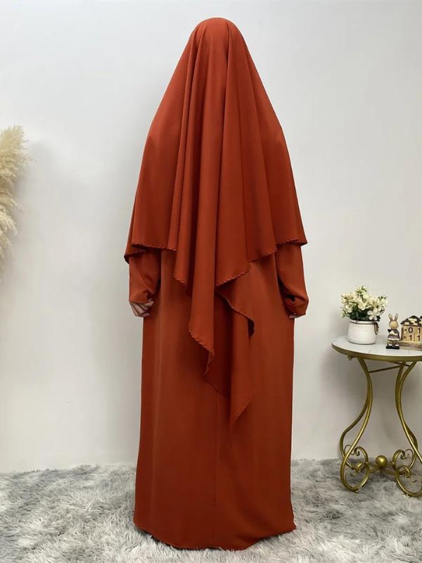 Femme portant un khimar long orange terre brûlée, vue de dos, posant dans un intérieur minimaliste 