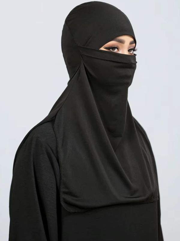 Niqab à capuche noir Nuit de Taïf vu de trois quarts sur une abaya noire, voile sous les yeux et plastron souple sur la poitrine
