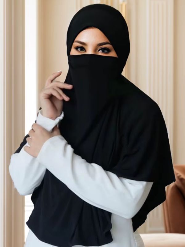 Niqab une pièce noir Nuit du Hedjaz porté de face, main près du voile, capuche et cape en jersey sur un haut blanc