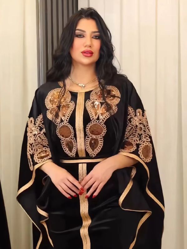 Une femme porte une robe caftan noire, devant un miroir